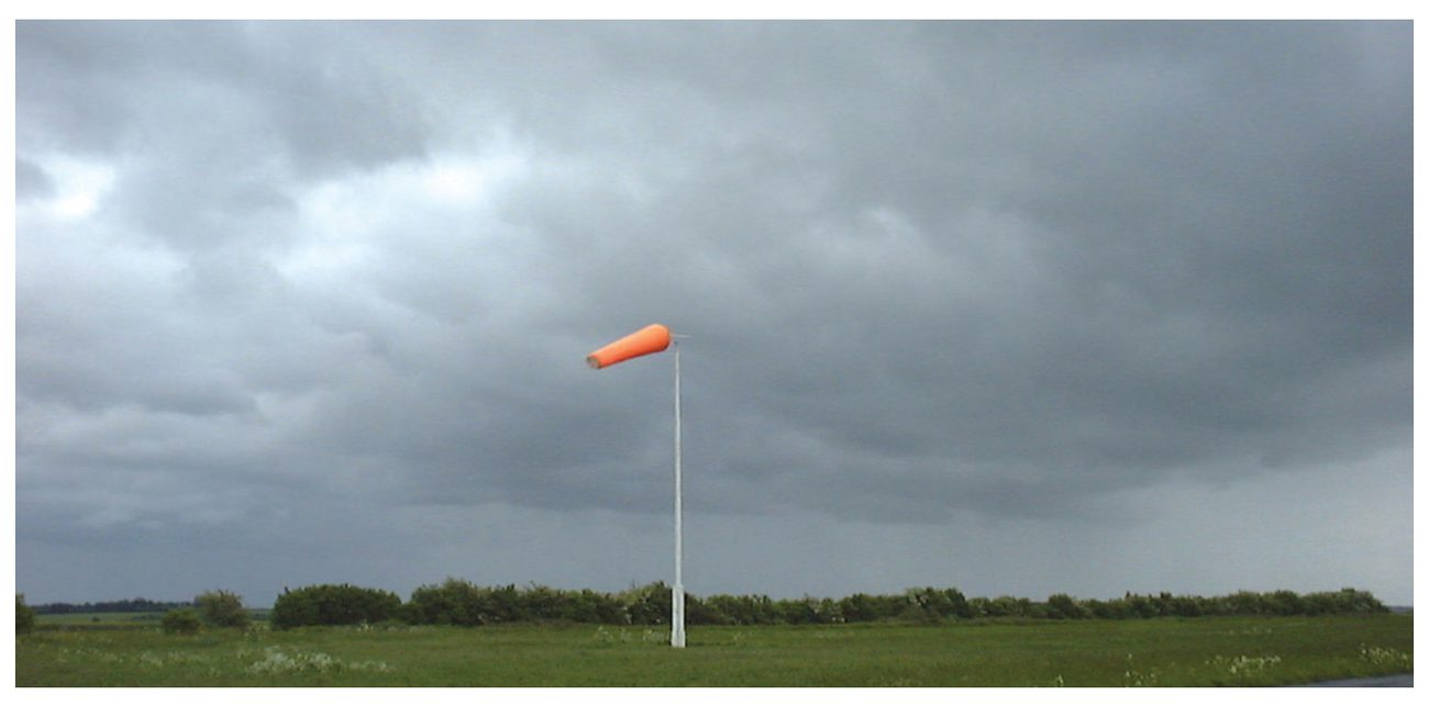 Photograph of a thick, dark grey nimbostratus layer over open ground with a windsock in the foreground.
